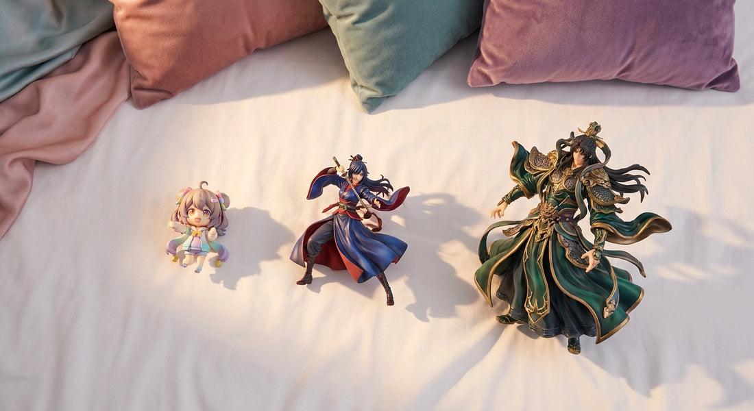 Three anime collectible figures of varying sizes and styles arranged side by side on a clean white surface under warm editorial lighting, representing chibi, scale, and statue figure types.