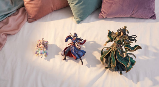 Three anime collectible figures of varying sizes and styles arranged side by side on a clean white surface under warm editorial lighting, representing chibi, scale, and statue figure types.